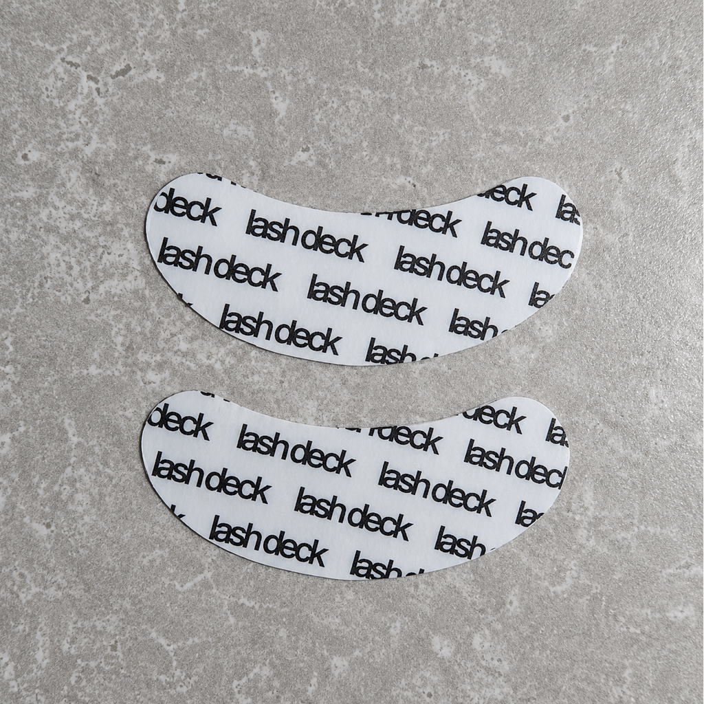 Two white eye patches with 'lash deck' text on a gray surface