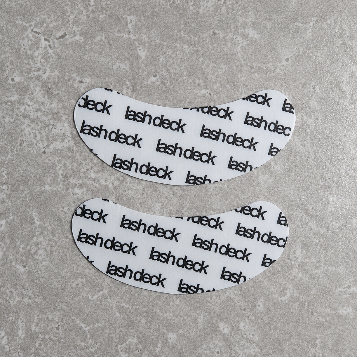 Two white eye patches with 'lash deck' text on a gray surface